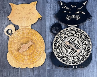 May include: Two wooden cat-shaped game boards with a spinning wheel. The wheel has numbers 1-32 and a fish design. One board is light brown and the other is black.
