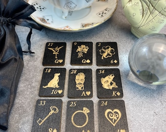 May include: A set of nine black wooden cards with gold accents and illustrations. Each card has a number, a suit, and a unique image. The cards are arranged in a grid pattern on a gray surface.