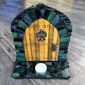 May include: A small wooden door with a green and blue mosaic frame, a yellow wooden door with a metal knob and a symbol, and a white candle on a black base.
