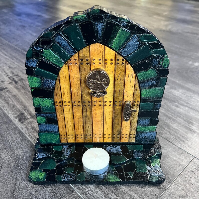 May include: A small wooden door with a green and blue mosaic frame, a yellow wooden door with a metal knob and a symbol, and a white candle on a black base.