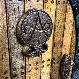 May include: A wooden door with a metal door knocker featuring a circular design with a swirl pattern. The door is made of wood planks and has a rustic look.