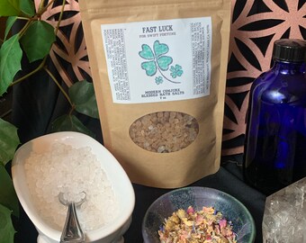 May include: A brown paper bag with a label that reads "Fast Luck for Swift Fortune" and a four-leaf clover design. The bag contains brown bath salts. The label also reads "Modern Conjure Blessed Bath Salts 7 oz".