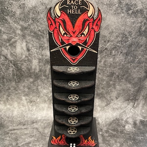 May include: A wooden game tower with a red devil face at the top. The tower has a black background with gold pentagrams and the words "Race to Hell". A black die with white dots is at the bottom of the tower.