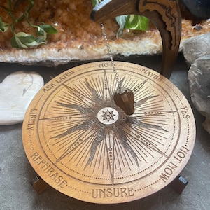 May include: Wooden decision making wheel with a pendulum. The wheel has the following options: Yes, Likely, Maybe, No, Ask Later, Rephrase, Unsure, and  Don't Know.