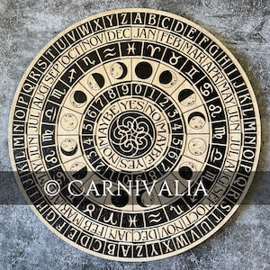 May include: A wooden circular board with a black and white design. The board features a calendar with the months of the year, zodiac signs, and moon phases. The center of the board has a black and white design with the word "CARNIVALIA" written in a decorative font.