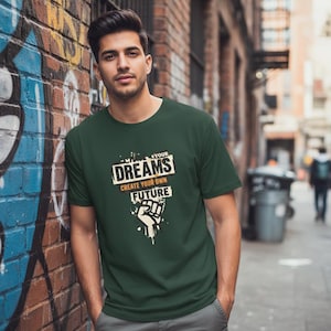 May include: Dark green t-shirt with the text "YOUR DREAMS CREATE YOUR OWN FUTURE" in a white and orange design. The design includes a clenched fist graphic. The shirt is short-sleeved and has a crew neck.