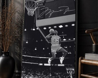 May include: Black and white framed print of a basketball player mid-air, about to shoot a ball. The player wears a red jersey with the number 23. The background shows a scoreboard and a crowd of people.