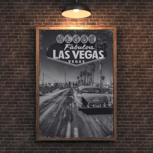 Puede incluir: Impresión en blanco y negro enmarcada del letrero de Las Vegas y un coche clásico en una carretera desértica. El letrero dice "Welcome Fabulous Las Vegas". La impresión se muestra en una pared de ladrillo.