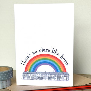 K&ouml;nnte beinhalten: Eine wei&szlig;e Karte mit einem Regenbogenbogen &uuml;ber einer Reihe von H&auml;usern. Der Text "There's no place like home" ist um den Regenbogenbogen geschrieben.