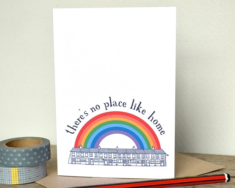 K&ouml;nnte beinhalten: Eine wei&szlig;e Karte mit einem Regenbogenbogen &uuml;ber einer Reihe von H&auml;usern. Der Text "There's no place like home" ist um den Regenbogenbogen geschrieben.