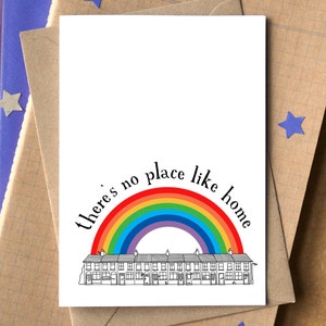 K&ouml;nnte beinhalten: Eine Gru&szlig;karte mit einem Regenbogen &uuml;ber einer Reihe von H&auml;usern und dem Text "Es gibt keinen Ort wie zu Hause".