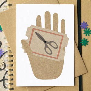 May include: A greeting card showing a hand holding a ticket with scissors. The hand and ticket are brown, with a red border around the ticket. The scissors are grey. The card is on a notebook with flower cutouts.