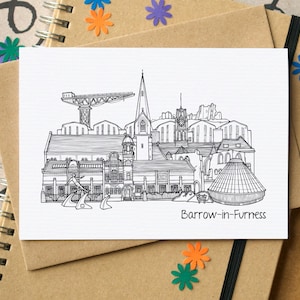 May include: A monochrome line drawing of Barrow-in-Furness, depicting buildings, a crane, and a church spire. The text "Barrow-in-Furness" is printed beneath the illustration. The drawing is on a white card, resting on a brown notebook.