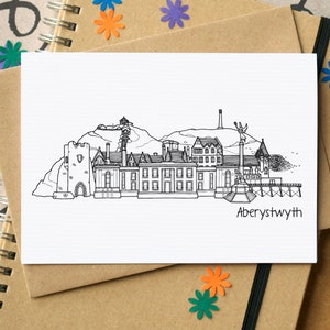 Rectangular landscape white greetings card with brown envelope. The card shows a black and white line drawing of Aberystwyth skyline buildings and has the word Aberystwyth; bottom right below the illustration.