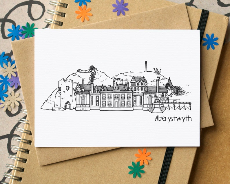 Rectangular landscape white greetings card with brown envelope. The card shows a black and white line drawing of Aberystwyth skyline buildings and has the word Aberystwyth; bottom right below the illustration.