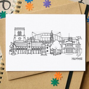 May include: Black and white line drawing illustration of the Hatfield skyline, featuring a church, a large building with a dome, and other buildings. The text "Hatfield" is at the bottom of the image.