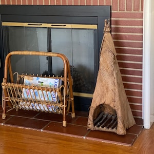 May include: A brick fireplace with a black metal screen and a wicker magazine rack. The rack is filled with magazines and is sitting on the hearth. There is a wooden sculpture on the right side of the fireplace.