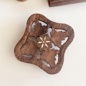 May include: A brown wooden coaster with a carved floral design. The center of the coaster features a white star-shaped inlay.