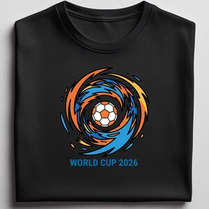 May include: Black crew neck t-shirt featuring a soccer ball graphic at the center, surrounded by orange, yellow, and blue swirling lines. The text "WORLD CUP 2026" is printed below the graphic in blue. The shirt is made of a soft material.