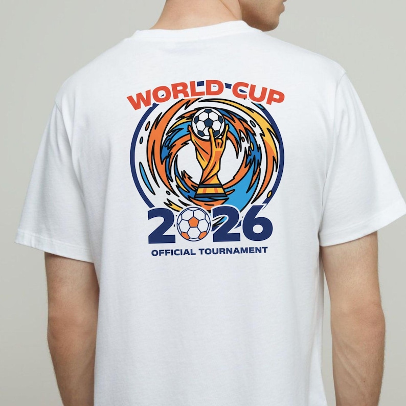 May include: White t-shirt with a colorful graphic on the back. The design features the words "WORLD CUP" in red, a soccer ball, and the number "2026" in blue. The shirt also includes the text "OFFICIAL TOURNAMENT".