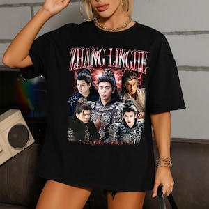 May include: Black t-shirt featuring a graphic of five people with ornate clothing and the text "ZHANG LINGHE" in a red, distressed font. The design has a vintage, retro style.