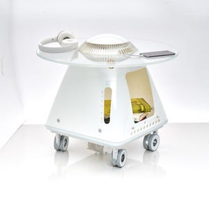 May include: A contemporary white side table with a clear glass top. The table has a distinctive design with a rounded base and four wheels. White headphones, a lamp, and a smartphone are on the table. The table is approximately 61 cm tall.