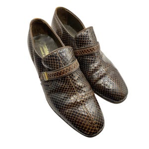 May include: A pair of vintage brown leather shoes with a snakeskin pattern. The shoes have a strap with a buckle and a rounded toe. The shoes are in good condition and appear to be well-made.