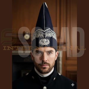 Pode incluir: Um homem usando um uniforme azul escuro, incluindo um chapéu alto e pontudo com acabamento branco e um emblema prateado. O uniforme também apresenta um casaco escuro e uma gola branca. O fundo mostra painéis de madeira.