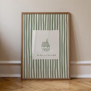 May include: A framed print featuring a green and white striped background. The center has a white square with a line drawing of a house and the text "this house gon' love itself" in a handwritten font. The frame is a light brown color.