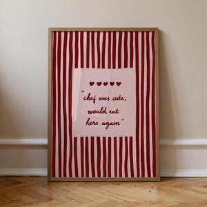 Puede incluir: Impresión enmarcada con un fondo a rayas rojas y blancas. La impresión presenta un cuadrado rosa claro con el texto "chef was cute, would eat here again" y cuatro símbolos de corazón.