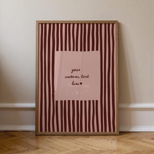 Può includere: Una stampa artistica incorniciata con uno sfondo a righe rosa e bordeaux. Il centro presenta un rettangolo rosa con il testo "your custom text here" in stile scritto a mano, con un simbolo a cuore. La cornice è in legno.