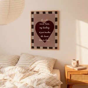 May include: A framed print with the text "the cold never lasts, my darling it just teaches the heart how to burn." The print features a burgundy heart on a mauve background, framed with a black and white checkered border.