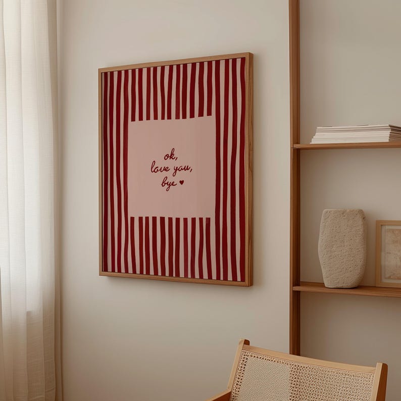 May include: A framed art print with a wooden frame. The artwork features a pink square with the text "ok, love you, bye." in cursive, surrounded by vertical red stripes on a white background.