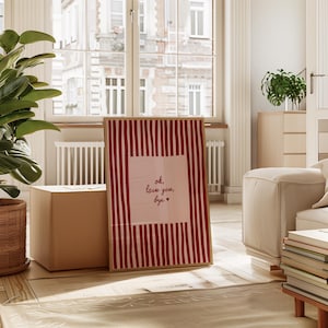 May include: A framed art print with a red and white striped background and the text "ok, love you, bye" in a handwritten style. The print is displayed in a bright, airy room with natural light and a neutral color palette.
