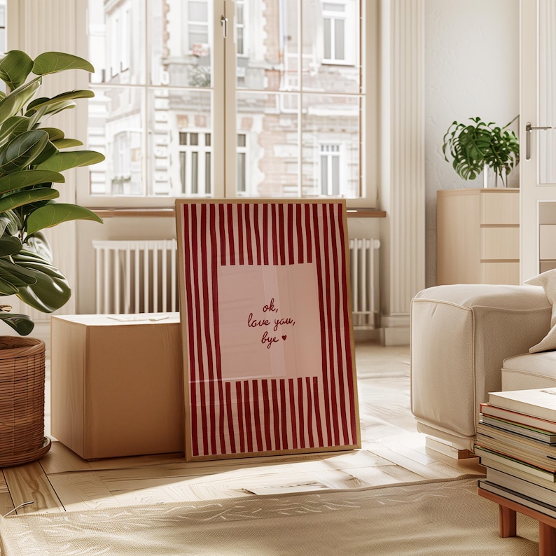 May include: A framed art print with a red and white striped background and the text "ok, love you, bye" in a handwritten style. The print is displayed in a bright, airy room with natural light and a neutral color palette.