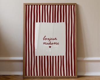 May include: Framed art print with a red and white striped background. The center features a white square with the words "bonjour madame" in red script, and a small red heart. The frame is a light brown color.