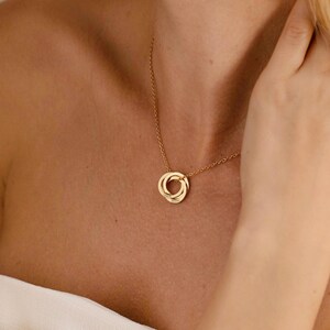 May include: A gold necklace with three intertwined rings as a pendant. The chain is fine and the pendant sits on a person's chest. The necklace is a simple, elegant piece of jewellery.