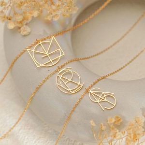 以下が含まれることがあります： 3つの金色の幾何学的なペンダントネックレス。各ネックレスは、正方形、円、ひし形など、異なる抽象的なデザインが特徴です。ネックレスは、ドライフラワーのある明るい色の表面に表示されています。
