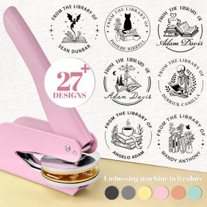 May include: A pink embossing machine with a gold and silver die, surrounded by circular stamp designs. The stamps feature illustrations of books, cats, and other library-themed elements. Text on the image reads "27+ Designs" and "Embossing machine in 6 colors."