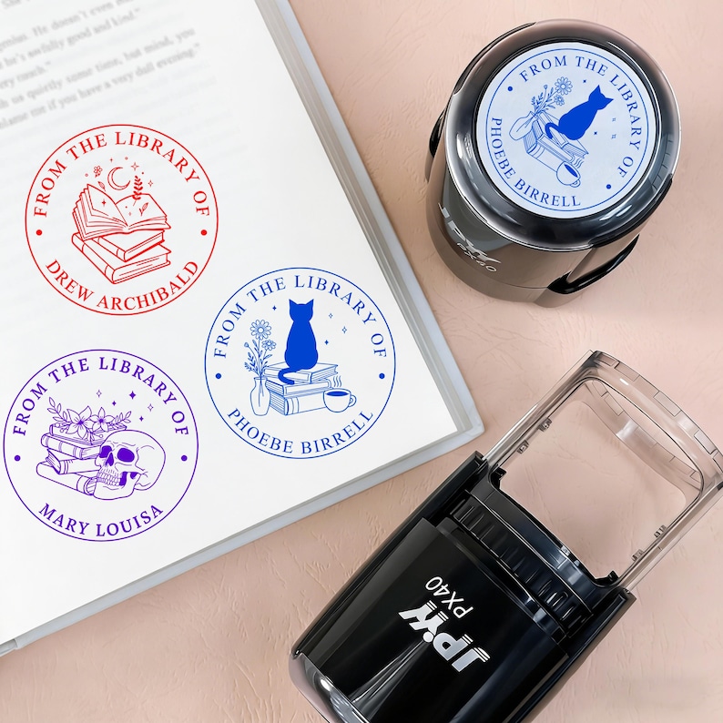 May include: A collection of library stamps with various designs, including a cat, books, and a skull. The stamps are in red, blue, and purple ink. One stamp is in use, and the others are on a white surface.