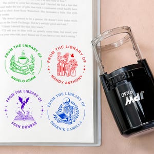 May include: A black self-inking stamp next to a page with four custom library stamps. The stamps feature circular designs with text and illustrations, including books, flowers, and a skeleton reading. The stamp is labeled "PX40".
