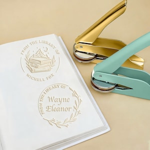 May include: A gold and a teal library seal sit next to a white book with embossed text. The book has two embossed library seals with the text "From the Library of" and names. The gold seal is open, and the teal seal is closed.