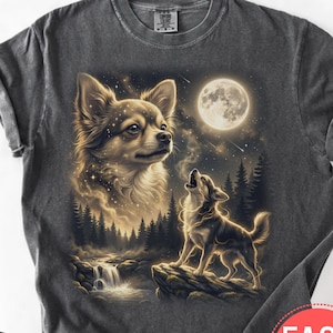 Pode incluir: Camiseta cinza escuro com uma ilustração detalhada de um Chihuahua e um cão uivando sob a lua cheia. O design inclui uma floresta, uma cachoeira e um céu estrelado. A camisa tem uma lavagem vintage e gola redonda.