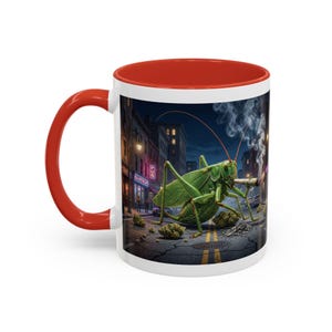 Puede incluir: Taza de cerámica blanca con interior y asa rojos. La taza presenta una ilustración detallada de un gran saltamontes verde fumando un cigarrillo en una calle de la ciudad por la noche. La taza tiene un diseño único y llamativo.