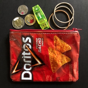 May include: A red Doritos Fromage Nacho Cheese bag repurposed as a zippered pouch, with coins, a green USB drive, and rubber bands. The pouch features the Doritos logo and images of tortilla chips.