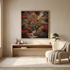 May include: A framed landscape painting depicts a river winding through a forest with autumn foliage. The artwork is displayed above a wooden console table, with a small bonsai tree and a cream-colored armchair with a blanket.