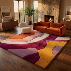 Può includere: Un tappeto rettangolare caratterizzato da un motivo astratto multicolore con forme organiche fluide in tonalità magenta intenso, arancione bruciato, giallo senape, rosa tenue e crema, realizzato con una superficie a pelo spesso e strutturato.