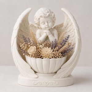 May include: A white resin sculpture of a cherub with closed eyes and hands clasped in prayer, framed by two large wings. The cherub sits behind a fluted bowl filled with dried flowers, including cream-colored roses, lavender sprigs, and grasses.