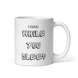 May include: White ceramic mug with the text "I WORK WHILE YOU SLEEP" in black, outlined letters. The mug has a standard handle and a glossy finish. The mug is designed for hot beverages.