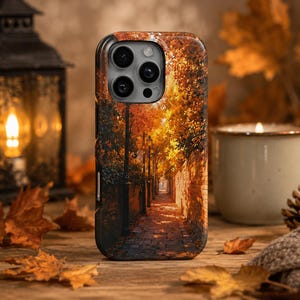 Puede incluir: Una funda para smartphone con una imagen impresa de un estrecho camino de adoquines bordeado por muros de ladrillo y farolas altas, rodeado de árboles otoñales con follaje naranja y amarillo bajo una luz cálida y dorada en otoño.